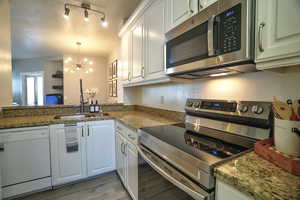 Kitchen featuring stainless steel appliances, hanging lights, white cabinetry, light stone counters, and light wood-style flooring