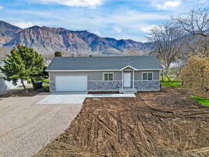 Ranch-style house with concrete driveway, a mountain view, stone siding, roof with shingles, and a garage