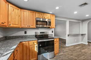 Kitchen featuring stainless steel appliances, dark stone countertops, recessed lighting, and dark wood-style flooring