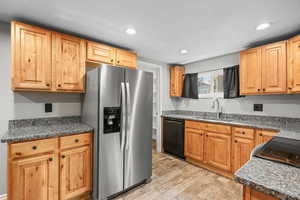 Kitchen with black appliances, light wood finished floors, recessed lighting, and dark stone counters