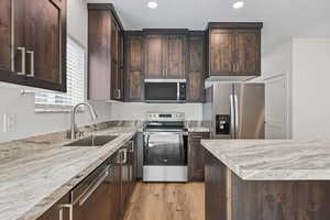 Kitchen featuring dark wood finish cabinetry, stainless steel appliances, light wood finished floors, recessed lighting, and light stone counters