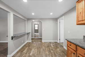 Kitchen with arched walkways, wood finish floors, recessed lighting, and dark stone countertops