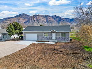 Ranch-style house featuring driveway, stone siding, a mountain view, an attached garage, and roof with shingles