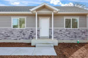 Doorway to property with stone siding and a shingled roof