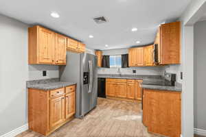Kitchen with stainless steel appliances, dark stone countertops, light wood-style flooring, and recessed lighting