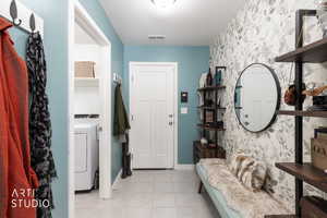 Entrance foyer with washer / dryer, light tile patterned floors, and wallpapered walls
