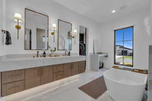 Full bathroom featuring double vanity, a freestanding tub, a walk in closet, recessed lighting, and light marble finish flooring