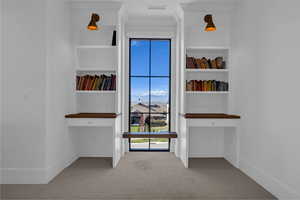 Corridor with light colored carpet, built in shelves, and a desk