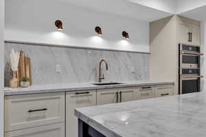Kitchen featuring light stone counters, double oven, and white cabinets