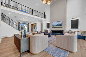 Living room featuring a high ceiling, light wood-style flooring, suspended lighting, and a glass covered fireplace