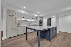 Dual tone kitchen with light stone counters, a kitchen island, light wood-style floors, decorative backsplash, and a breakfast bar