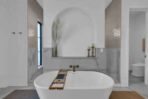 Bathroom with marble tiled flooring, a soaking tub, and tile walls
