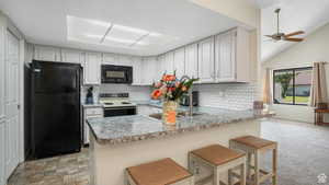 Kitchen with black appliances, a breakfast bar, a peninsula, light countertops, and vaulted ceiling