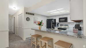 Kitchen featuring a breakfast bar area, black appliances, a peninsula, decorative backsplash, and light carpet