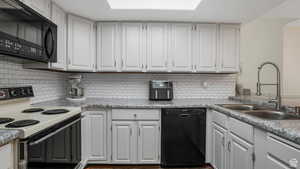 Kitchen featuring black appliances, white cabinets, light countertops, and tasteful backsplash