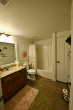 Bathroom with vanity, shower / bath combo with shower curtain, dark tile patterned floors, and a textured ceiling
