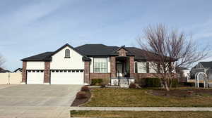 View of front facade with a front yard, an attached garage, brick siding, and driveway