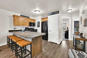 Kitchen featuring black appliances, a peninsula, a breakfast bar area, dark wood finished floors, and refinished countertops
