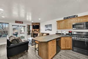 Kitchen featuring stainless steel appliances, open floor plan, a kitchen breakfast bar, a peninsula, and a stone fireplace