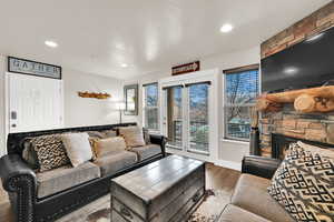 Living room with wood finished floors, a stone fireplace, and recessed lighting