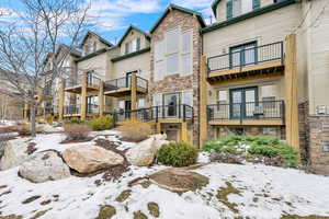 Snow covered house featuring stone siding and a balcony