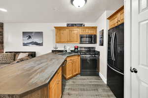 Kitchen featuring a peninsula, black appliances, light wood-style floors, open floor plan, and refinished countertops