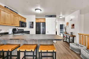 Kitchen featuring a peninsula, black appliances, light wood finished floors, a kitchen breakfast bar, refinished countertops