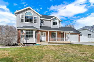 Traditional-style home with covered porch, brick siding, a shingled roof, and an attached garage