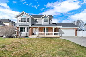 Traditional-style home with covered porch, a front yard, brick siding, roof with shingles, and driveway