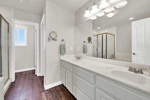 Full bathroom with double vanity, a shower stall, dark wood-style flooring, and a bath