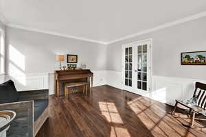 Sitting room featuring french doors, ornamental molding, wainscoting, dark wood-style flooring, and a decorative wall
