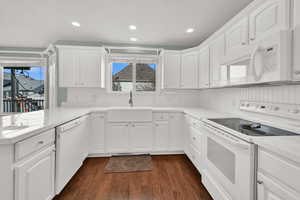 Kitchen with white appliances, white cabinetry, dark wood-style flooring, recessed lighting, and a peninsula