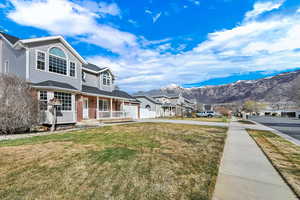View of property exterior featuring covered porch, brick siding, driveway, a mountain view, and a lawn