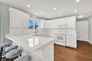 Kitchen with a breakfast bar area, white appliances, a peninsula, white cabinetry, and recessed lighting