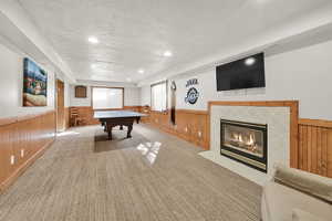 Game room with a fireplace, wainscoting, wooden walls, light colored carpet, and a textured ceiling