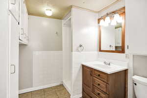 Bathroom featuring a textured ceiling, vanity, tile walls, a stall shower, and light tile patterned floors