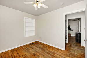 Empty room with built in features, wood-type flooring, and ceiling fan
