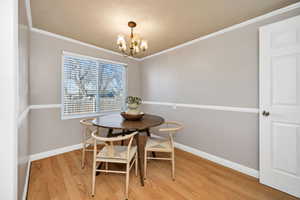 Dining area with light wood finished floors, a textured ceiling, a chandelier, and crown molding