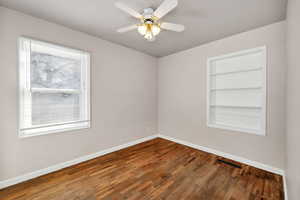 Unfurnished room with built in shelves, dark wood-style flooring, and ceiling fan