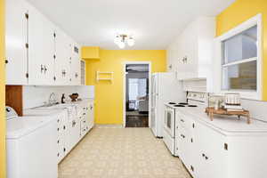Kitchen featuring washer / dryer, white appliances, open shelves, light countertops, and light floors