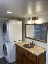 Bathroom featuring vanity, stacked washer and clothes dryer, and dark tile patterned floors