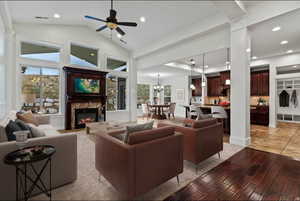 Living area with light wood-style floors, a ceiling fan, suspended lighting, a glass covered fireplace, and lofted ceiling