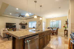 Kitchen featuring a fireplace, an island with sink, stainless steel appliances, open floor plan, and a ceiling fan