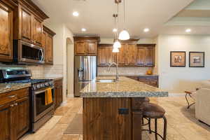 Kitchen featuring stainless steel appliances, pendant lighting, a kitchen breakfast bar, a kitchen island with sink, and tasteful backsplash