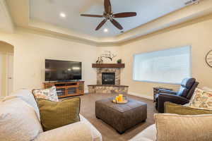Carpeted living area with ceiling fan, arched walkways, a raised ceiling, a fireplace, and recessed lighting