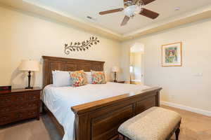 Bedroom with light carpet, arched walkways, ensuite bathroom, a ceiling fan, and a raised ceiling
