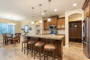 Kitchen featuring arched walkways, stainless steel appliances, light stone countertops, a kitchen bar, and backsplash