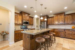Kitchen featuring arched walkways, a kitchen breakfast bar, wood finish cabinetry, a center island with sink, and decorative light fixtures