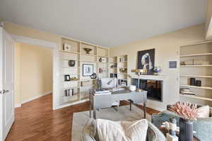 Home office with wood finished floors, built in shelves, and a multi sided fireplace
