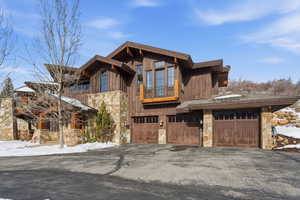 View of front of property featuring stone siding, a balcony, an attached garage, and asphalt driveway